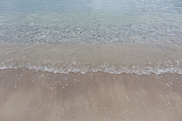Top view shot of soft wave licking sandy beach shore on cloudy day. Ocean scenery with calm translucent water and clean sand, a lot of copy space for text. Close up.