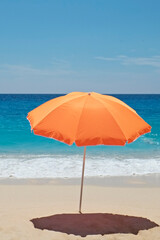 Single orange umbrella on a perfect beach with clean golden sand and clear turquoise water on a windless and sunny summer day. Tropical background, copy space, top view.