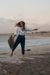 Young girl in a jumps on the oceanfront in blue jeans and white shirt, a brush in the hands and picture, near the water. 