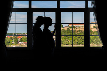 Fototapeta premium Silhouette of a young pregnant couple by the window.