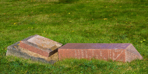 Obraz premium A broken grave marker. It is made from red granite, and has fallen over and is resting in the grass. There is room for text above.