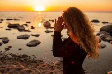 Profile of young woman relaxing on the beach, meditating with hands in Namaste gesture at sunset or...