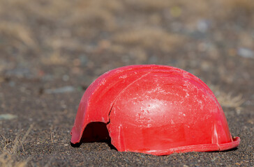 An old, broken hardhat lying on the ground. It is a faded and scratched red, and has a piece...