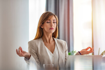 Young woman practicing meditation at the office desk. Young woman near the laptop, practicing meditation at the office desk, in front of laptop, online yoga classes
