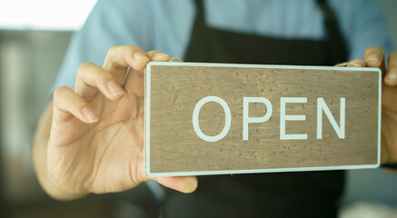 close up young business owner man holding open sign board to promote and inform reopening after...