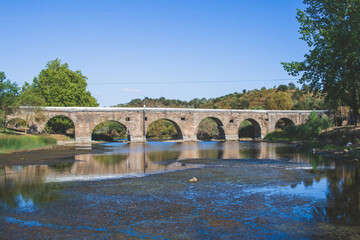 Naklejka premium Pillars of an old stone bridge over a dried riverbed in the summer. Empty river bed with poisoned muddy water with low water level. Prolonged drought. 