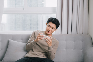 Asian young man is seriously playing the game on his smartphone on the couch.