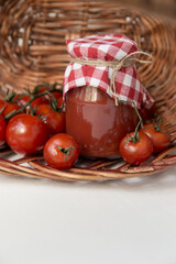 A jar of tomato sauce, ketchup or juice in a basket with tomatoes next to it