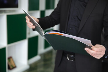 Businessman in black suit is holding a green book in his hands and checking up his business project...