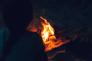 Fireplace on the beach at night. Little girl sitting near the fire with wood, flames in the nature at night.
