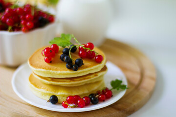 Summer breakfast pancakes with red and black currants in a bowl and milk in a glass jug on a white background