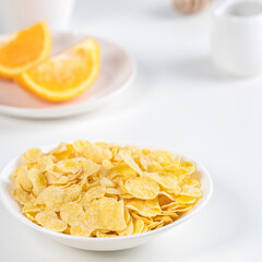 Corn flakes bowl sweeties with milk and orange on white background, close up, fresh and healthy breakfast design concept.