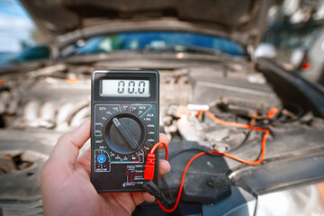 Man use multimeter with voltage range measurement to check up voltage level of the car battery. Man...