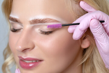 Blonde woman having permanent make-up tattoo on her eyebrows. Closeup beautician doing tattooing...