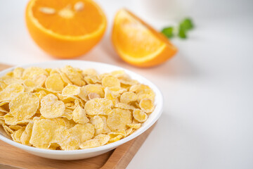 Corn flakes bowl sweeties with milk and orange on white background, close up, fresh and healthy breakfast design concept.