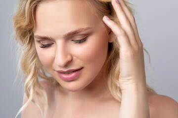 Fototapeta premium Beautiful smiling blonde woman with curly hair, clean skin and fresh make-up. She has beautiful blue eyes. Aesthetic cosmetology, hair treatment and makeup concept.