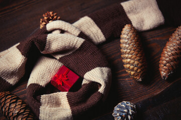 Fototapeta na wymiar Gift box and scarf with pine tree cones on wooden table