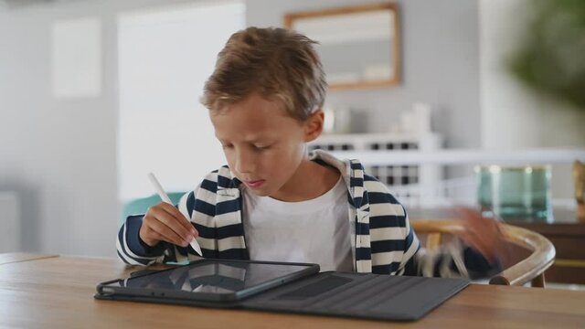 Child drawing picture with digital pen on tablet while looking at camera. Portrait of smiling cute kid using stylus on tablet to do homework for school. Artistic boy drawing on digital tablet.