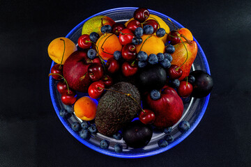 Still life of berries and fruit with blue illumination on a black background.