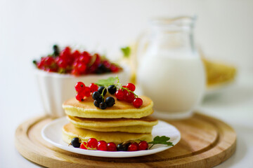 Summer breakfast pancakes with red and black currants in a bowl and milk in a glass jug on a white background