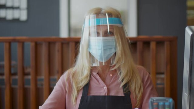 Senior Waitress In Medical Protective Mask And Plastic Face Shield Serving Restaurant