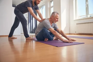 Rolgordijnen Mature yogi student exercising assisted by his coach © Svitlana