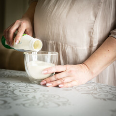 Pregnant woman pours kefir into a glass. Dairy product for health. Proper nutrition at 9 months of pregnancy. Healthy nutrition during quarantine.