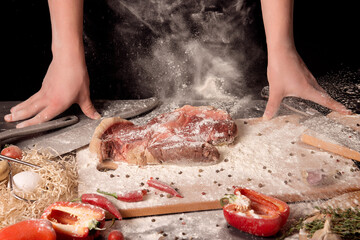 Raw beef steak on a kitchen board with flour and chili in front of the chef's hands.