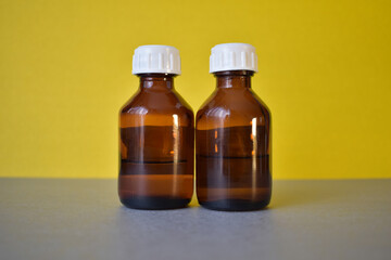 Two brown cosmetic bottles with a white lid on a gray-yellow background