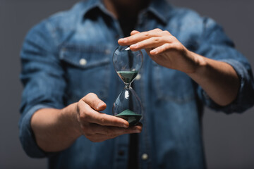 Cropped view of man holding hourglass with flowing sand isolated on grey, concept of time management