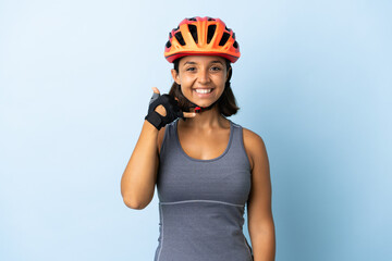 Young cyclist woman isolated on blue background making phone gesture. Call me back sign