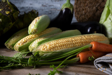 Fresh carrots with green tops, corn and eggplants on a wooden table