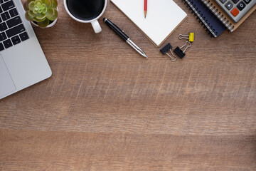 Top view above of wooden office desk table with laptop, notebook and coffee cup with equipment other office supplies.