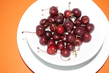 Las cerezas sobre un plato blanco con fondo naranja