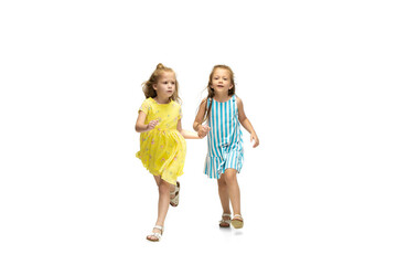 Happy children, little and emotional caucasian girls jumping and running isolated on white background. Looks happy, cheerful, sincere. Copyspace for ad. Childhood, education, happiness concept.