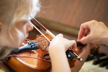 little girl with concentration plays on a small violin, suzuki lessons, learn flattens hand...