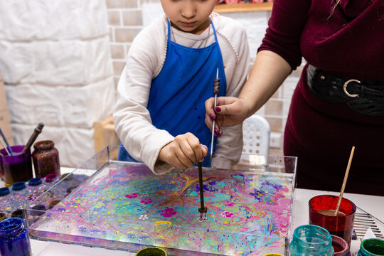 Ebru - Traditional art of origin from Turkey. The process of transferring an image to a sheet of paper. A 6-year-old girl is painting in the workshop with female artist, close up hands with tools.