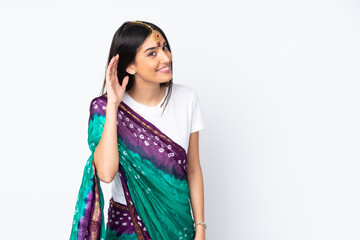 Young Indian woman isolated on white background listening to something by putting hand on the ear