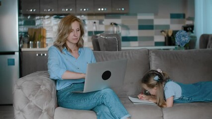 woman work with computer laptop while her daughter in painting on couch Rbbro. freelancer mom balancing lifestyle. multitasking. mother browsing internet and sitting with child