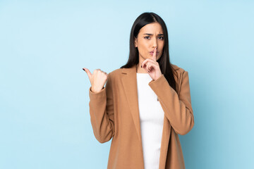 Young caucasian woman isolated on blue background pointing to the side and doing silence gesture