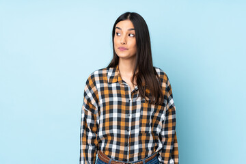 Fototapeta premium Young caucasian woman isolated on blue background making doubts gesture looking side
