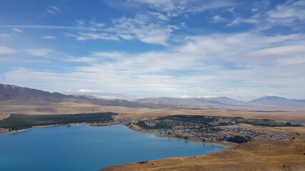lake Tekapo with mountains view, blue sky and white clouds in summer, with a small town (township) at the southern end of the lake, South Island, New Zealand