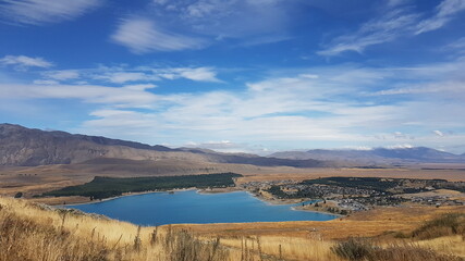 lake Tekapo with mountains view, blue sky and white clouds in summer, with a small town (township) at the southern end of the lake, South Island, New Zealand