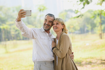 Photo portrait of Caucasian senior couple taking selfie photo with smartphone while enjoying moments of happiness in outdoors park on sunny day. Healthy senior or happy elder couple concept.