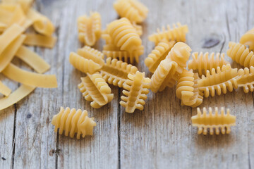 a lot of different kinds of egg noodles and yellow pasta on wooden background