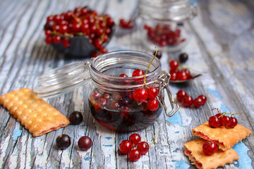 Delicious and healthy dessert. Glass jar with jam, red and black currant berries and cookies on a wooden table. Top view
