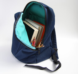 A blue backpack full of  books and colored pencils on a white background