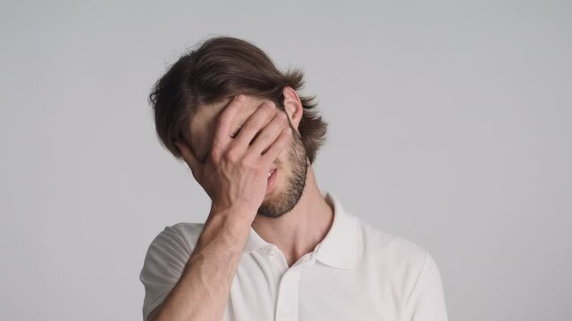 Portrait of young brunette man tiredly covering face and waving no gesture isolated. Face palm expression