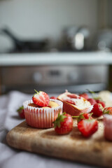 Strawberry muffins with fresh ripe berries on wooden board over kitchen table background