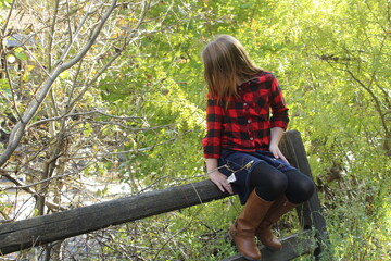 Girl wearing plaid and skirt sitting on fence looking at stream in Missoula Montana